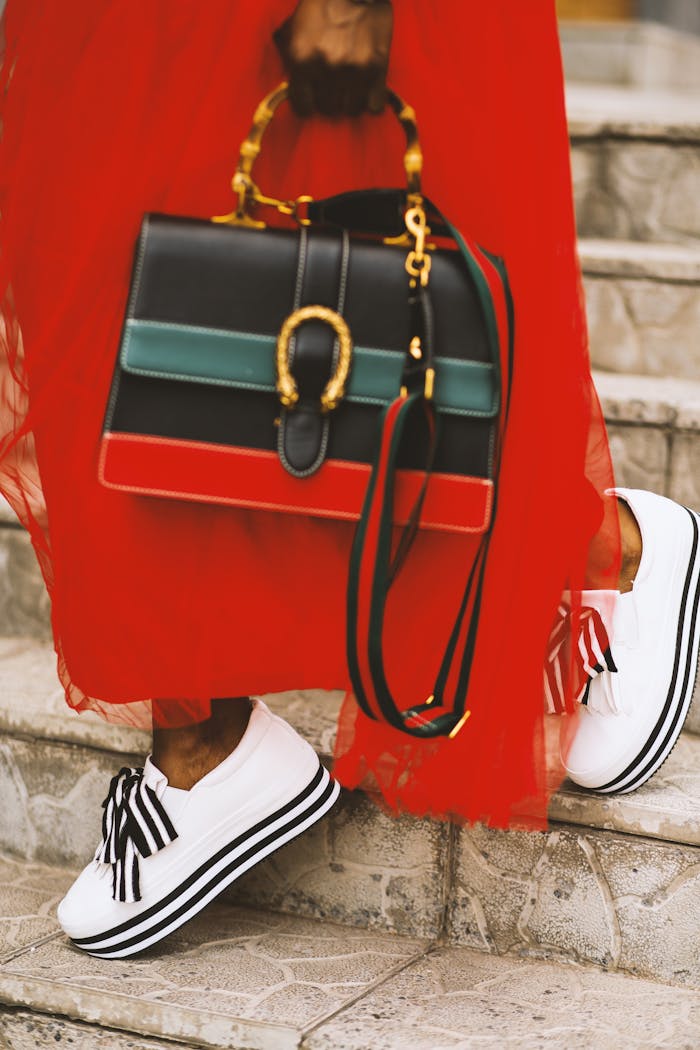 Fashionable woman in red dress with stylish bag and shoes on stairs.
